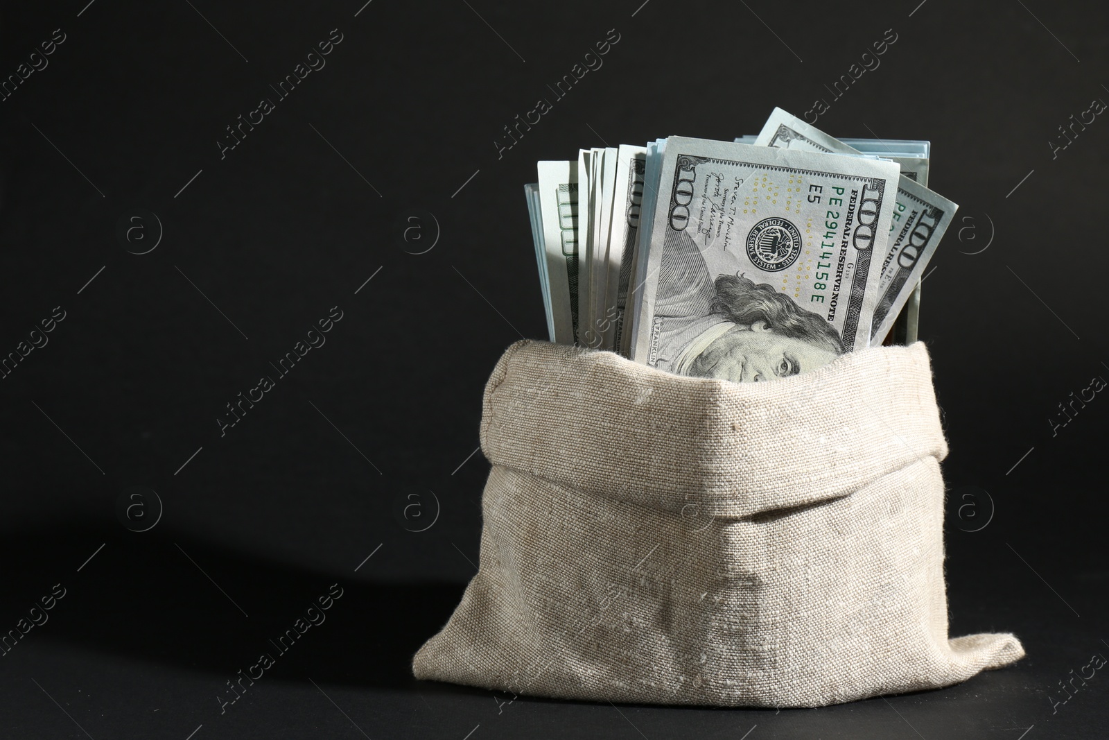 Photo of Dollar banknotes in burlap sack on dark background, space for text