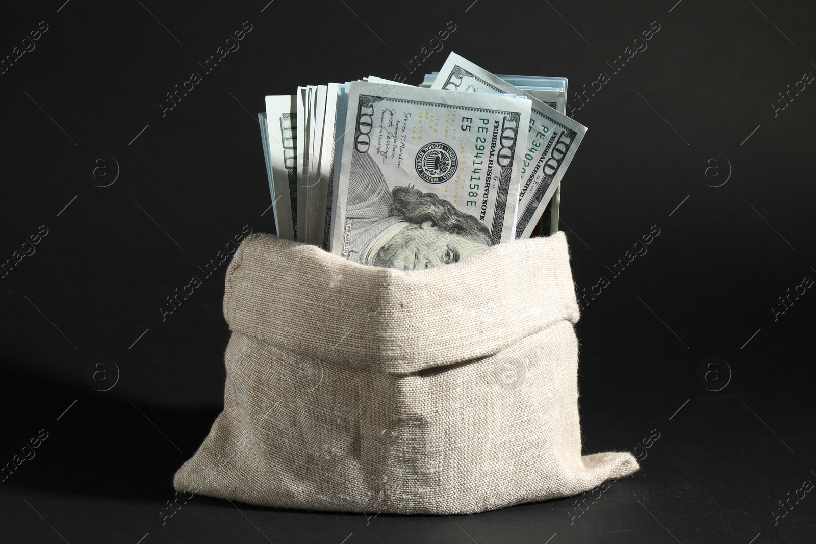 Photo of Dollar banknotes in burlap sack on dark background