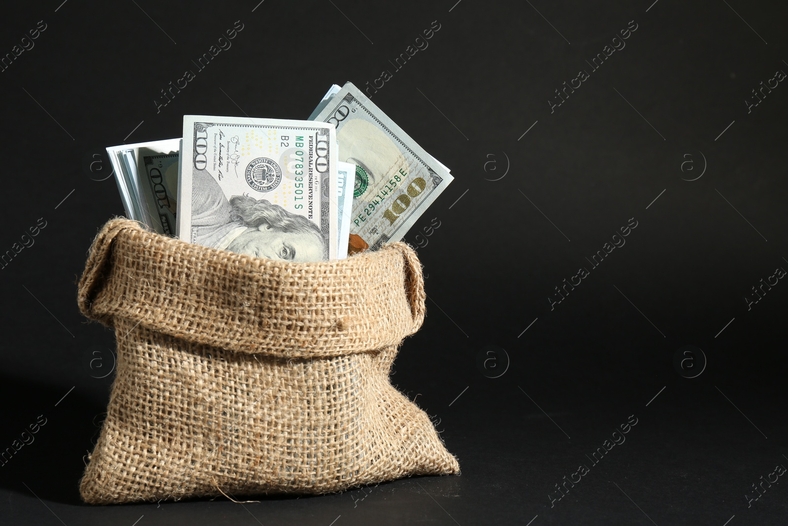 Photo of Dollar banknotes in burlap sack on dark background, space for text