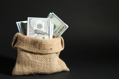 Photo of Dollar banknotes in burlap sack on dark background, space for text