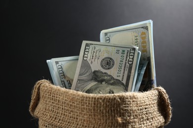 Photo of Dollar banknotes in burlap sack on dark background, closeup