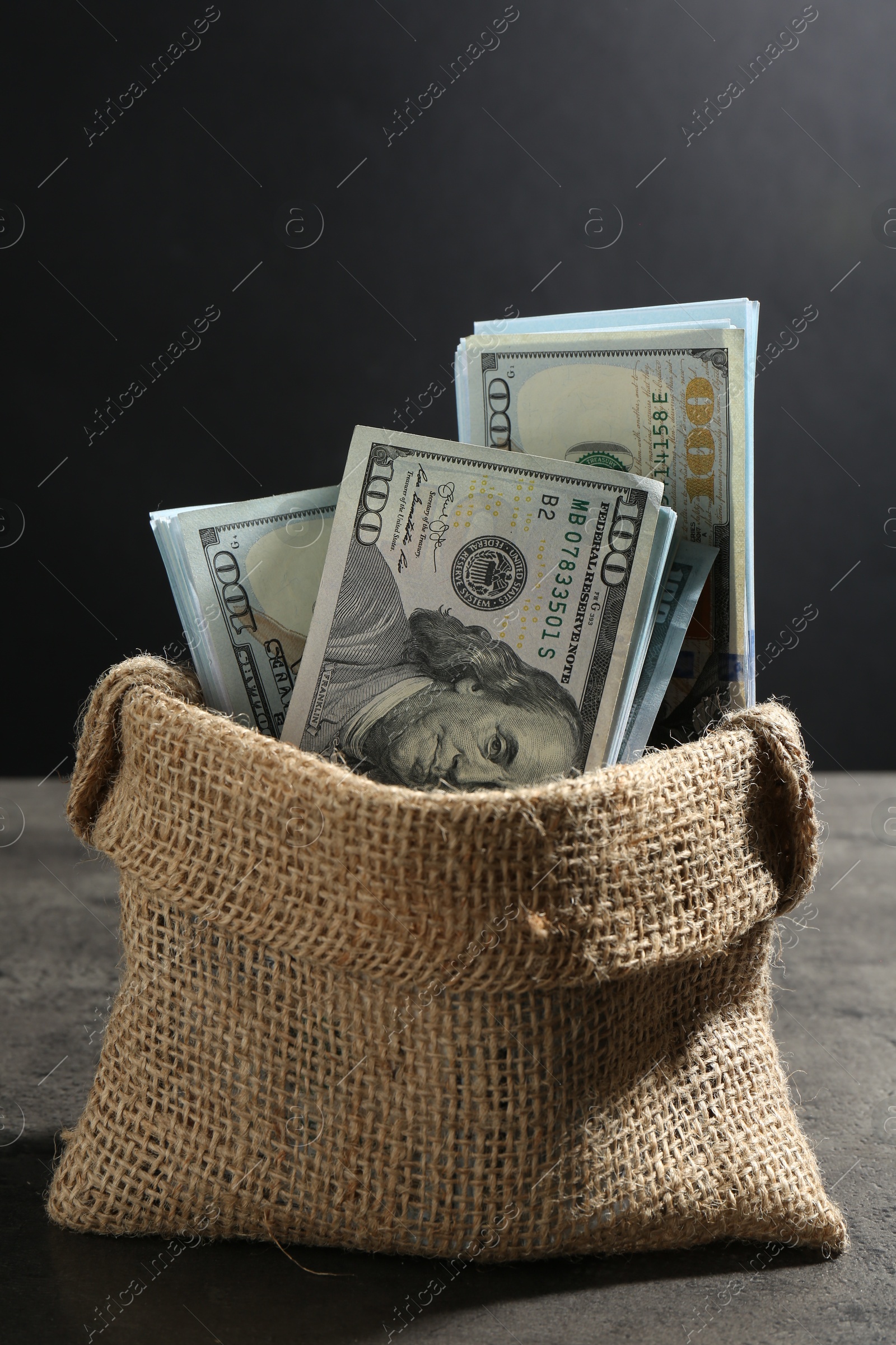 Photo of Dollar banknotes in burlap sack on grey table