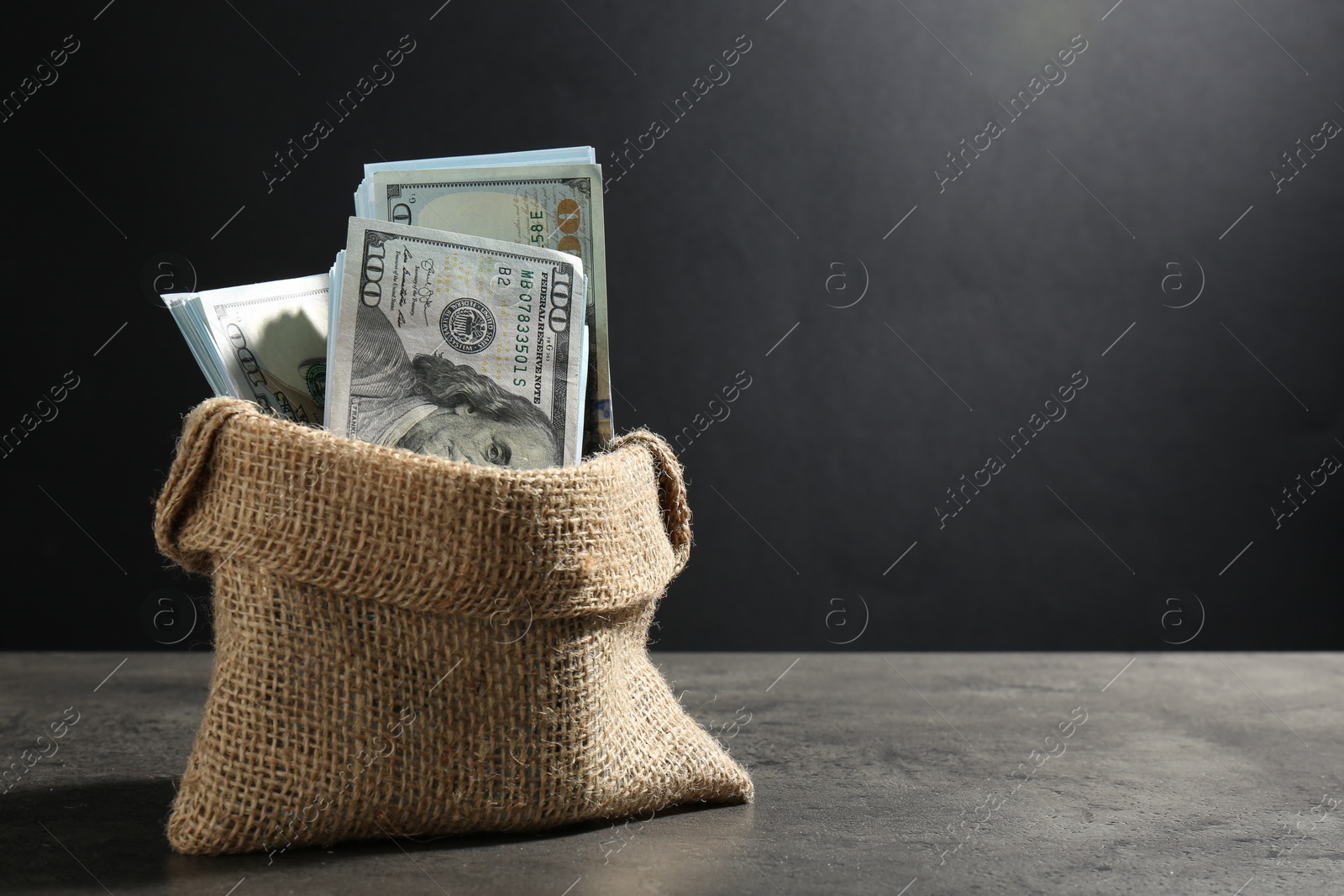 Photo of Dollar banknotes in burlap sack on grey table, space for text