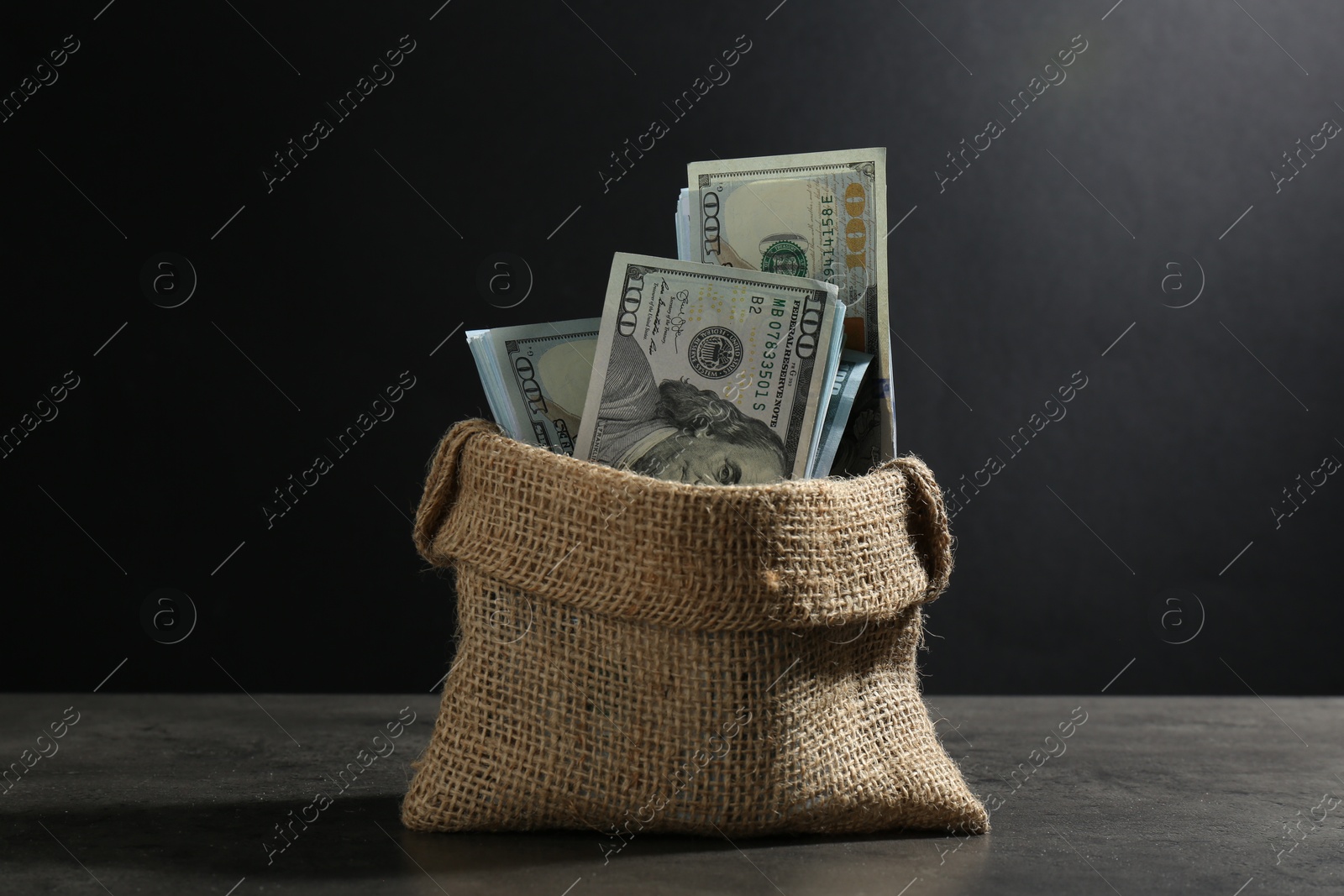 Photo of Dollar banknotes in burlap sack on grey table