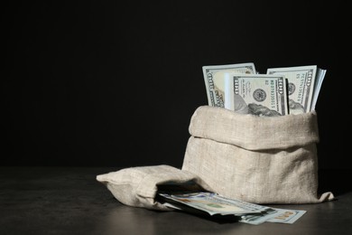 Photo of Dollar banknotes in burlap sacks on grey table against dark background, space for text