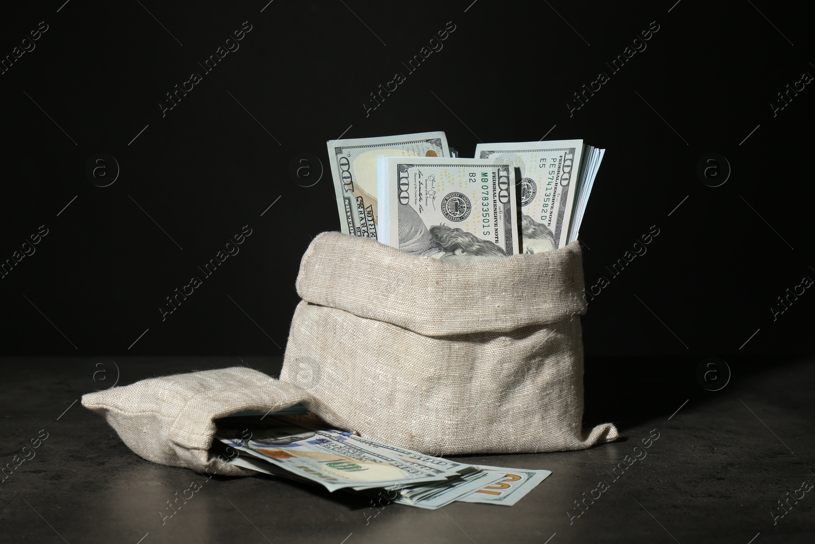 Photo of Dollar banknotes in burlap sacks on grey table against dark background