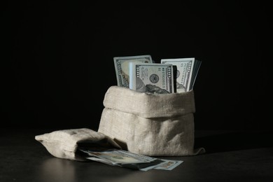 Photo of Dollar banknotes in burlap sacks on grey table against dark background