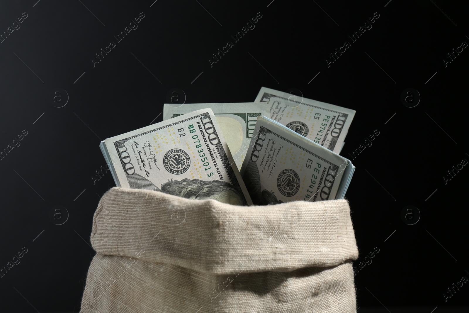 Photo of Dollar banknotes in burlap sack against black background, closeup