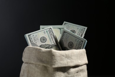 Photo of Dollar banknotes in burlap sack against black background, closeup