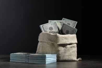 Photo of Dollar banknotes in burlap sack on grey table against dark background