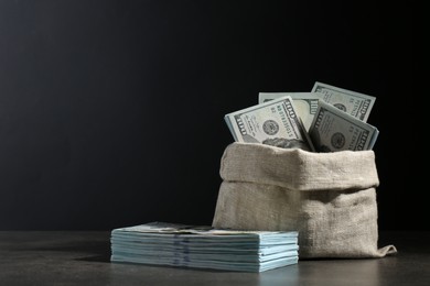 Photo of Dollar banknotes in burlap sack on grey table against dark background, space for text