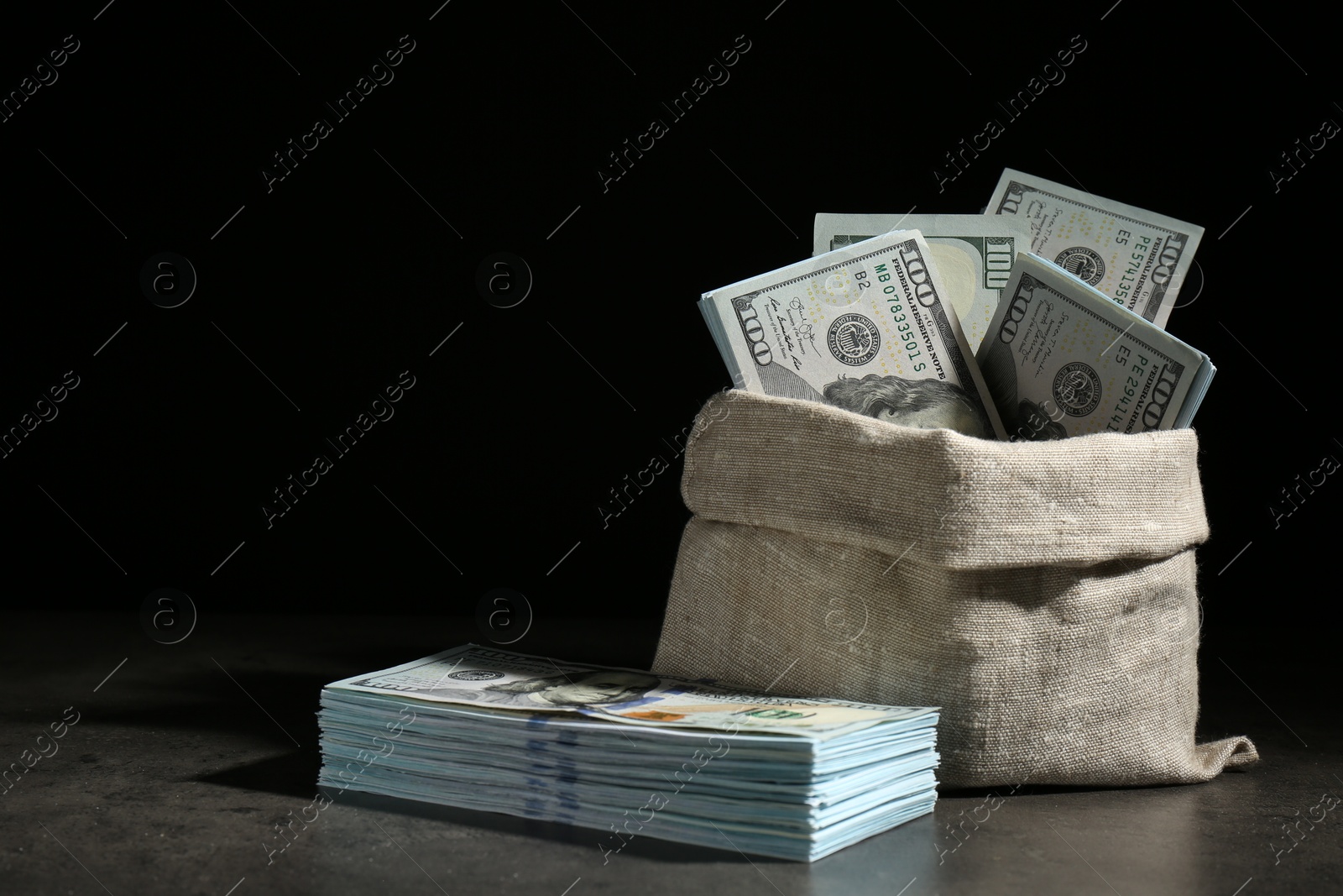 Photo of Dollar banknotes in burlap sack on grey table against dark background