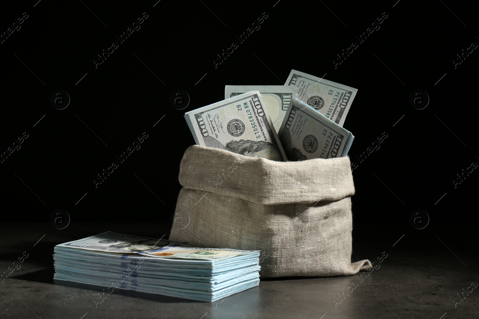 Photo of Dollar banknotes in burlap sack on grey table against dark background