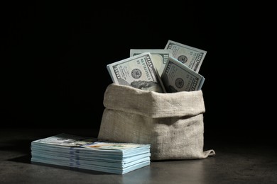 Photo of Dollar banknotes in burlap sack on grey table against dark background