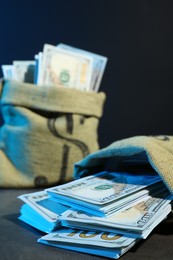 Photo of Dollar banknotes in burlap sacks on grey table against dark background in neon lights, closeup