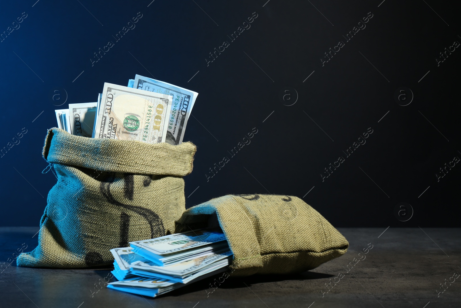 Photo of Dollar banknotes in burlap sacks on grey table against dark background in neon lights