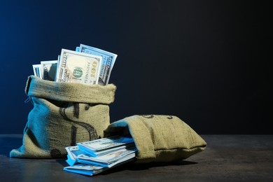 Photo of Dollar banknotes in burlap sacks on grey table against dark background in neon lights