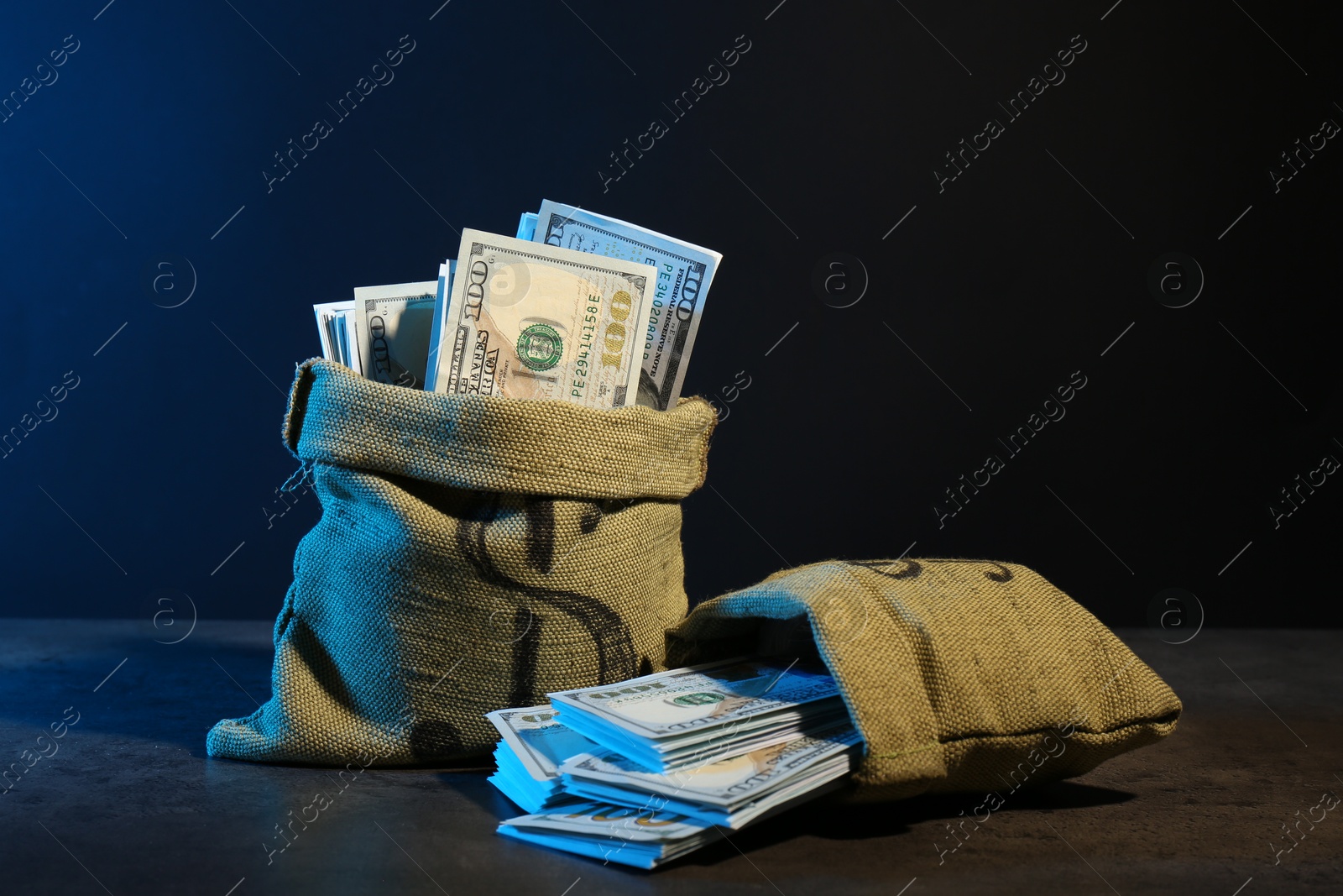 Photo of Dollar banknotes in burlap sacks on grey table against dark background in neon lights