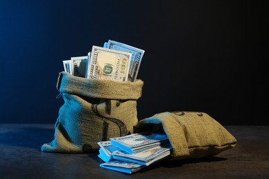 Photo of Dollar banknotes in burlap sacks on grey table against dark background in neon lights