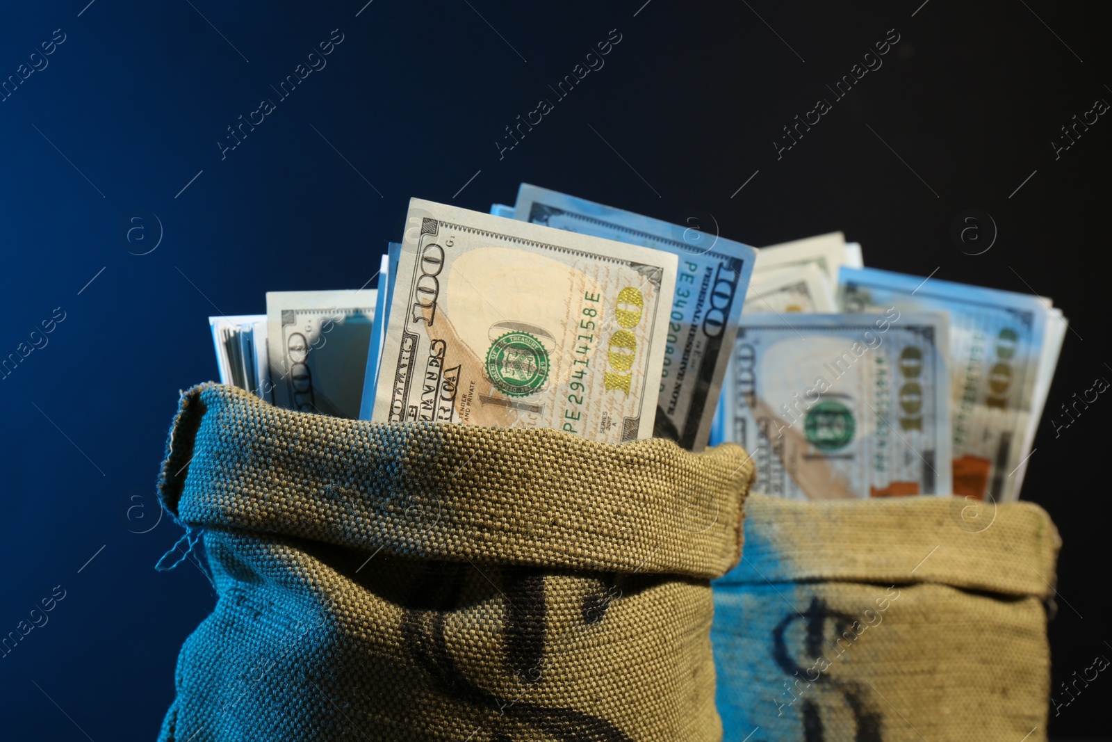 Photo of Dollar banknotes in burlap sacks against dark background in neon lights, closeup