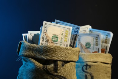 Photo of Dollar banknotes in burlap sacks against dark background in neon lights, closeup