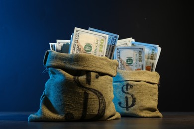 Photo of Dollar banknotes in burlap sacks on grey table against dark background in neon lights