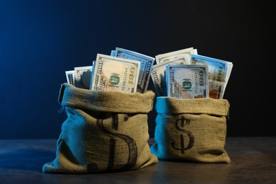 Photo of Dollar banknotes in burlap sacks on grey table against dark background in neon lights