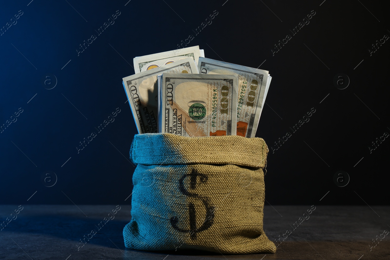 Photo of Dollar banknotes in burlap sack on grey table against dark background in neon lights