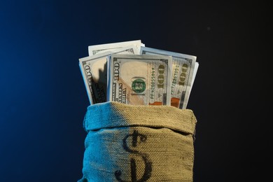 Photo of Dollar banknotes in burlap sack against dark background in neon lights, closeup