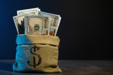 Photo of Dollar banknotes in burlap sack on grey table against dark background in neon lights, space for text