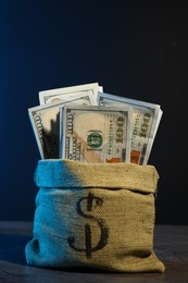 Photo of Dollar banknotes in burlap sack on grey table against dark background in neon lights