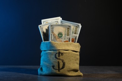 Photo of Dollar banknotes in burlap sack on grey table against dark background in neon lights