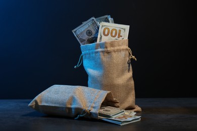 Photo of Dollar banknotes in burlap sacks on grey table against dark background in neon lights