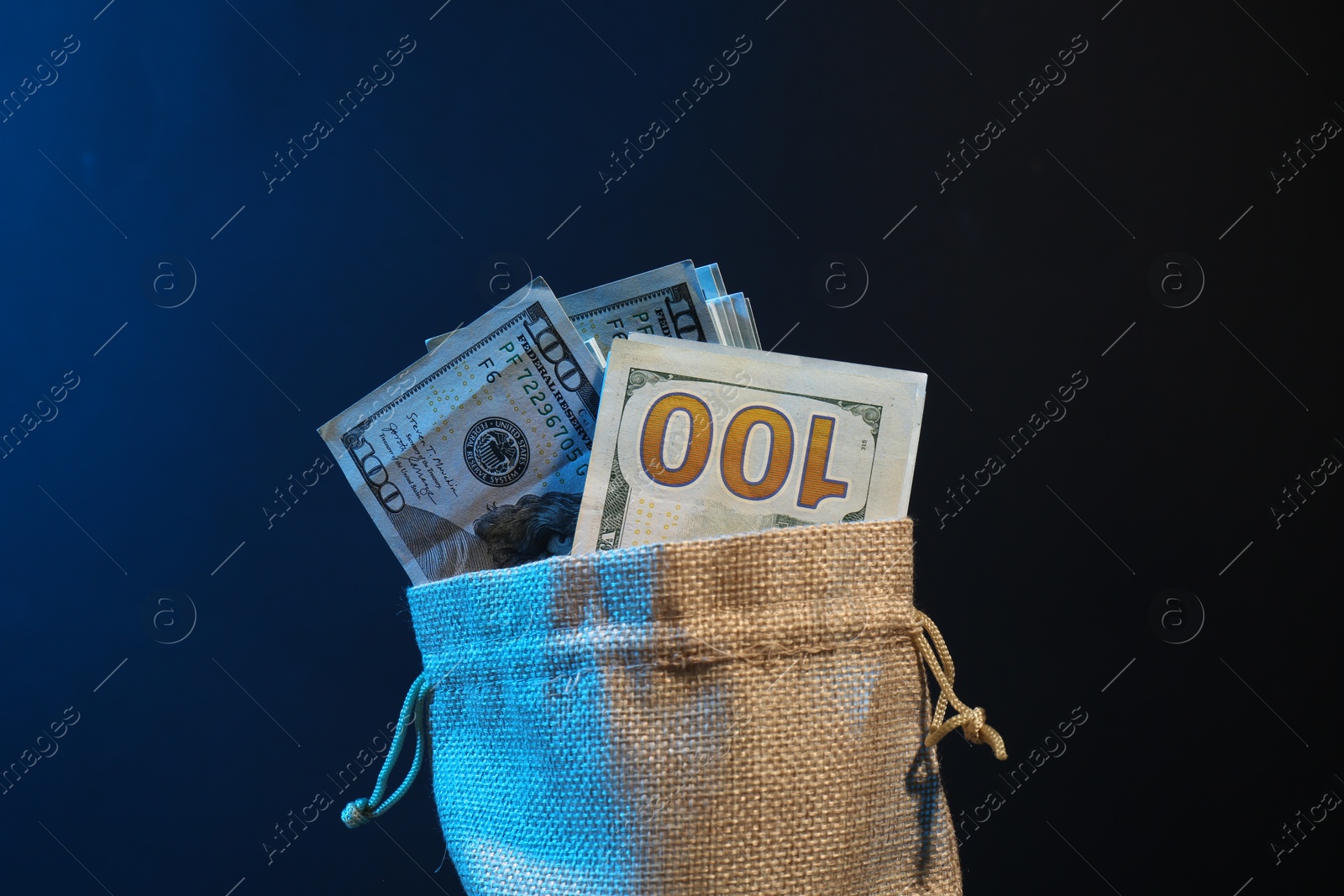 Photo of Dollar banknotes in burlap sack against dark background in neon lights, closeup