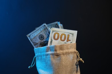 Photo of Dollar banknotes in burlap sack against dark background in neon lights, closeup