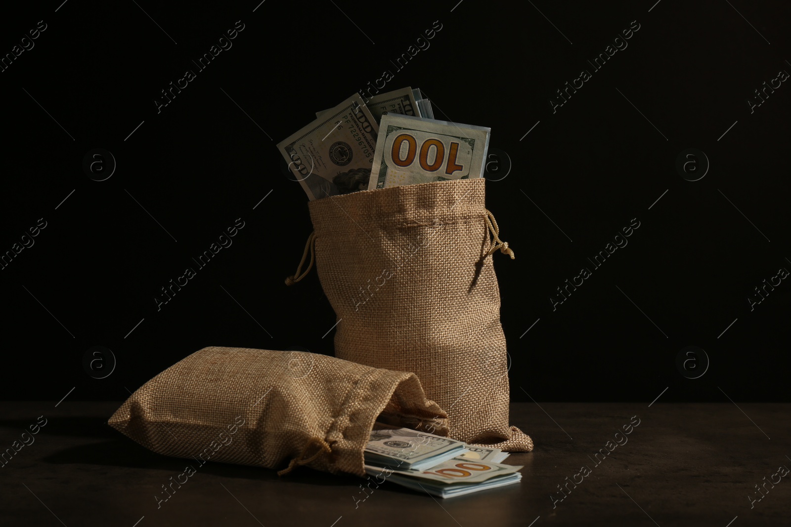 Photo of Dollar banknotes in burlap sacks on table against dark background