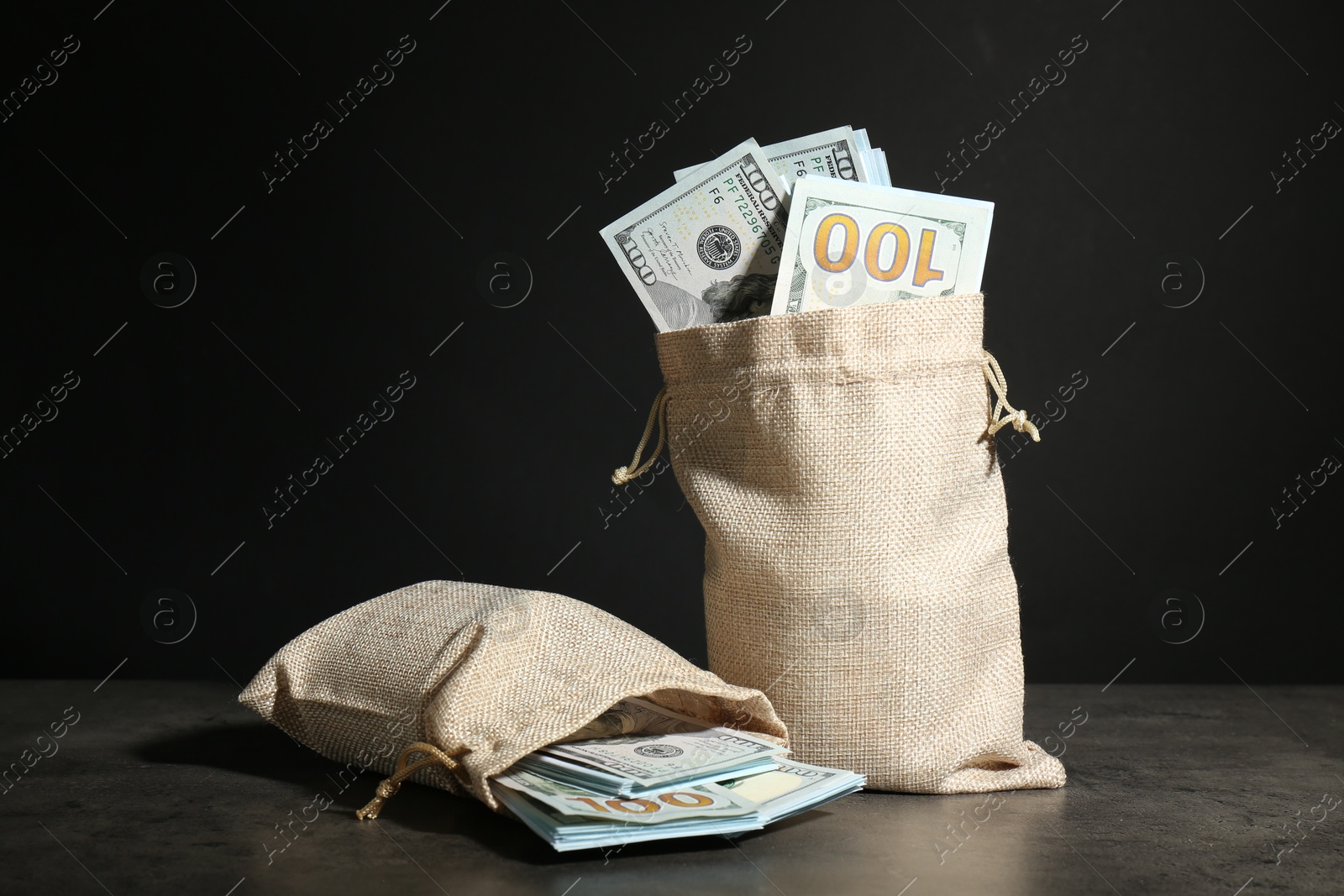 Photo of Dollar banknotes in burlap sacks on grey table against dark background