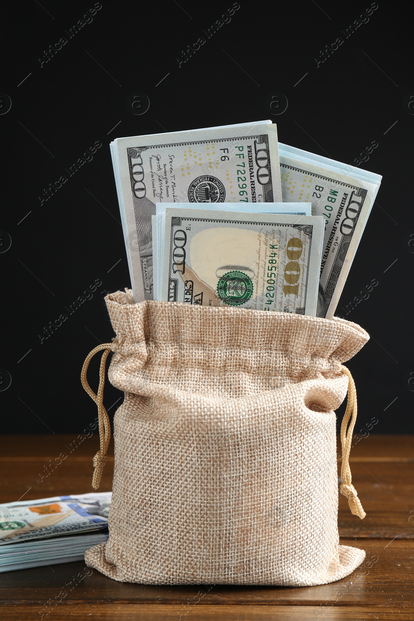 Photo of Dollar banknotes in burlap sack on wooden table against dark background