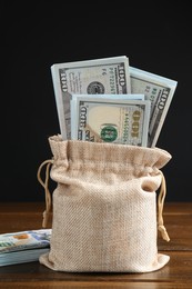 Photo of Dollar banknotes in burlap sack on wooden table against dark background