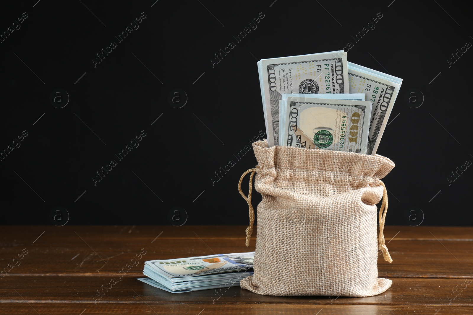 Photo of Dollar banknotes in burlap sack on wooden table against dark background