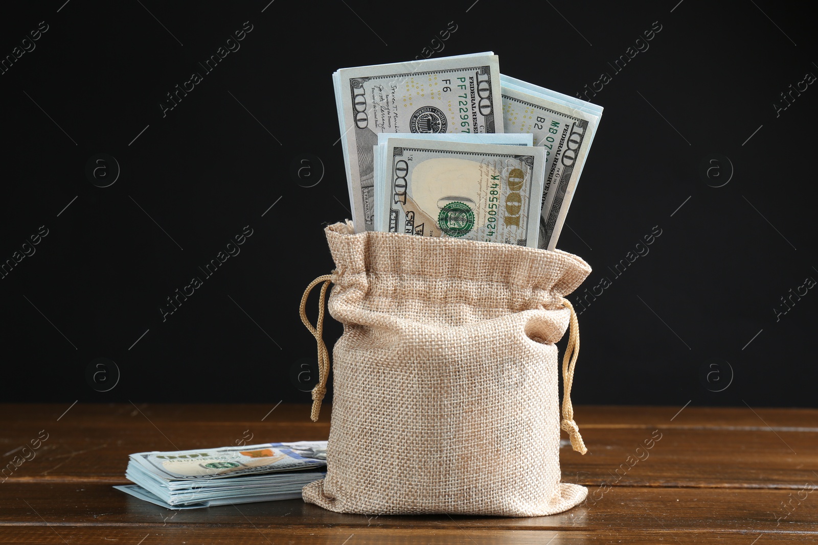 Photo of Dollar banknotes in burlap sack on wooden table against dark background