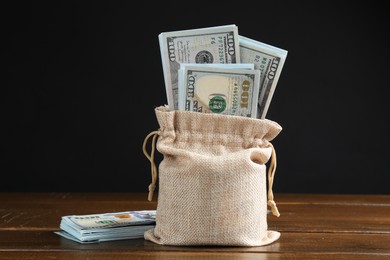 Dollar banknotes in burlap sack on wooden table against dark background