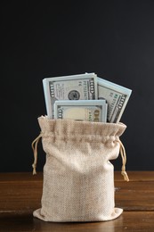 Photo of Dollar banknotes in burlap sack on wooden table against dark background