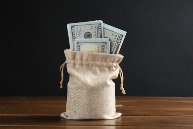 Photo of Dollar banknotes in burlap sack on wooden table against dark background