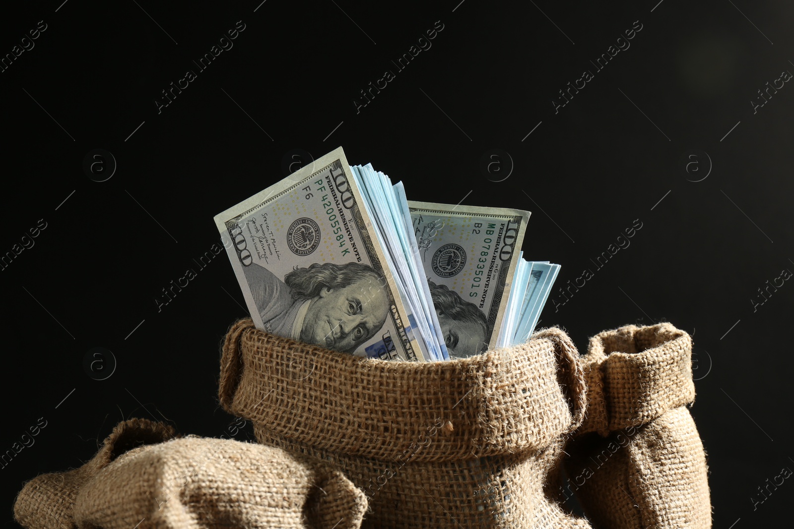 Photo of Dollar banknotes in burlap sacks against dark background, closeup