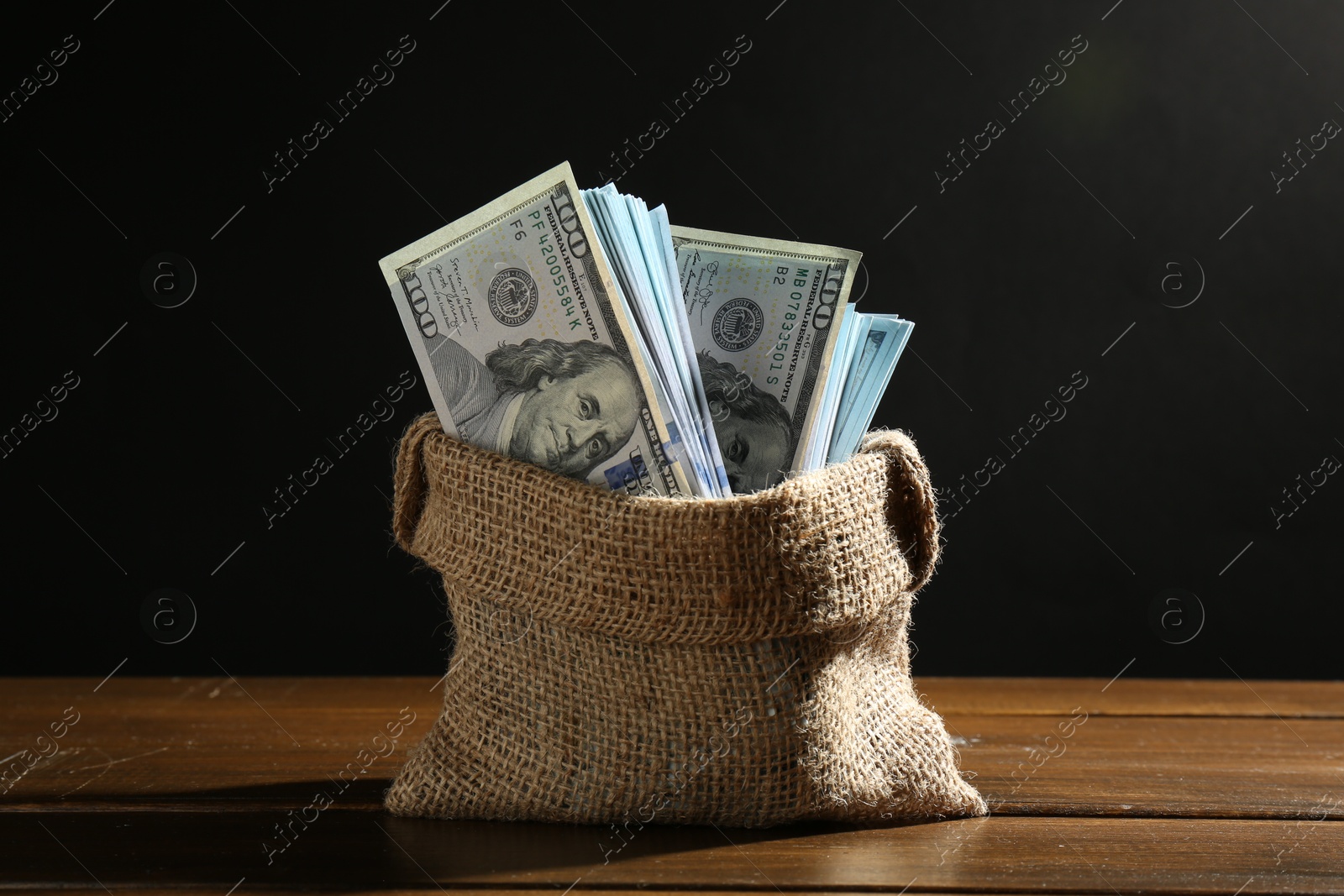 Photo of Dollar banknotes in burlap sack on wooden table against black background