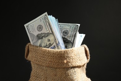 Photo of Dollar banknotes in burlap sack against black background, closeup