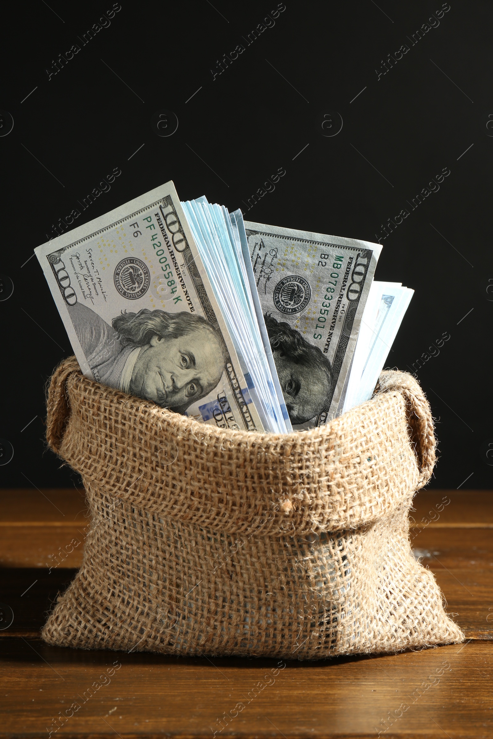 Photo of Dollar banknotes in burlap sack on wooden table against black background