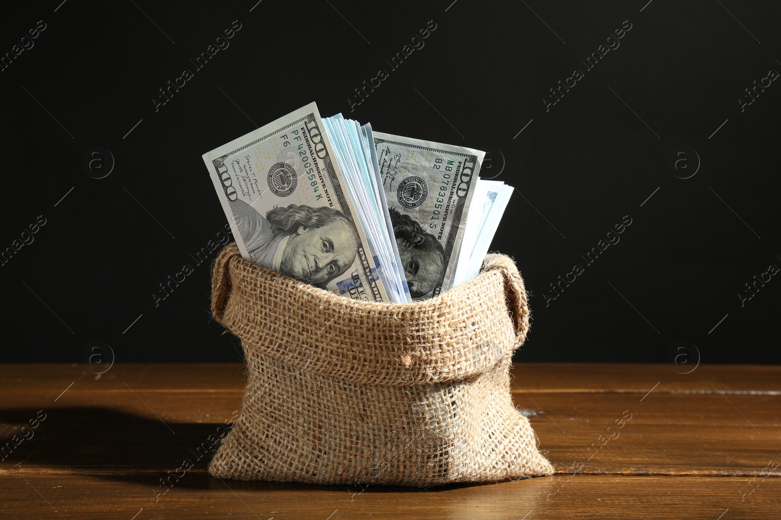 Photo of Dollar banknotes in burlap sack on wooden table against black background