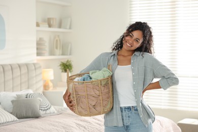 Photo of Happy woman with basket full of laundry in bedroom